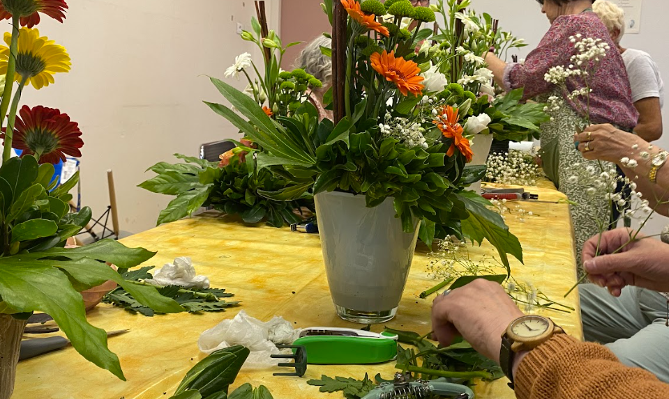 Photo de dame lors d'un atelier d'art floral, on y voit notamment des fleurs dans des pots. Il y a aussi une description de l'activité art floral.